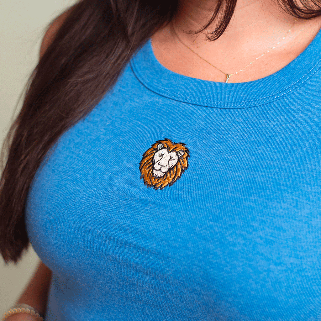 A close-up of a person wearing a honolulu blue tank top with a small embroidered lion head patch on the chest.