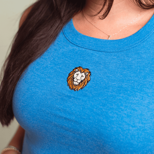 A close-up of a person wearing a honolulu blue tank top with a small embroidered lion head patch on the chest.
