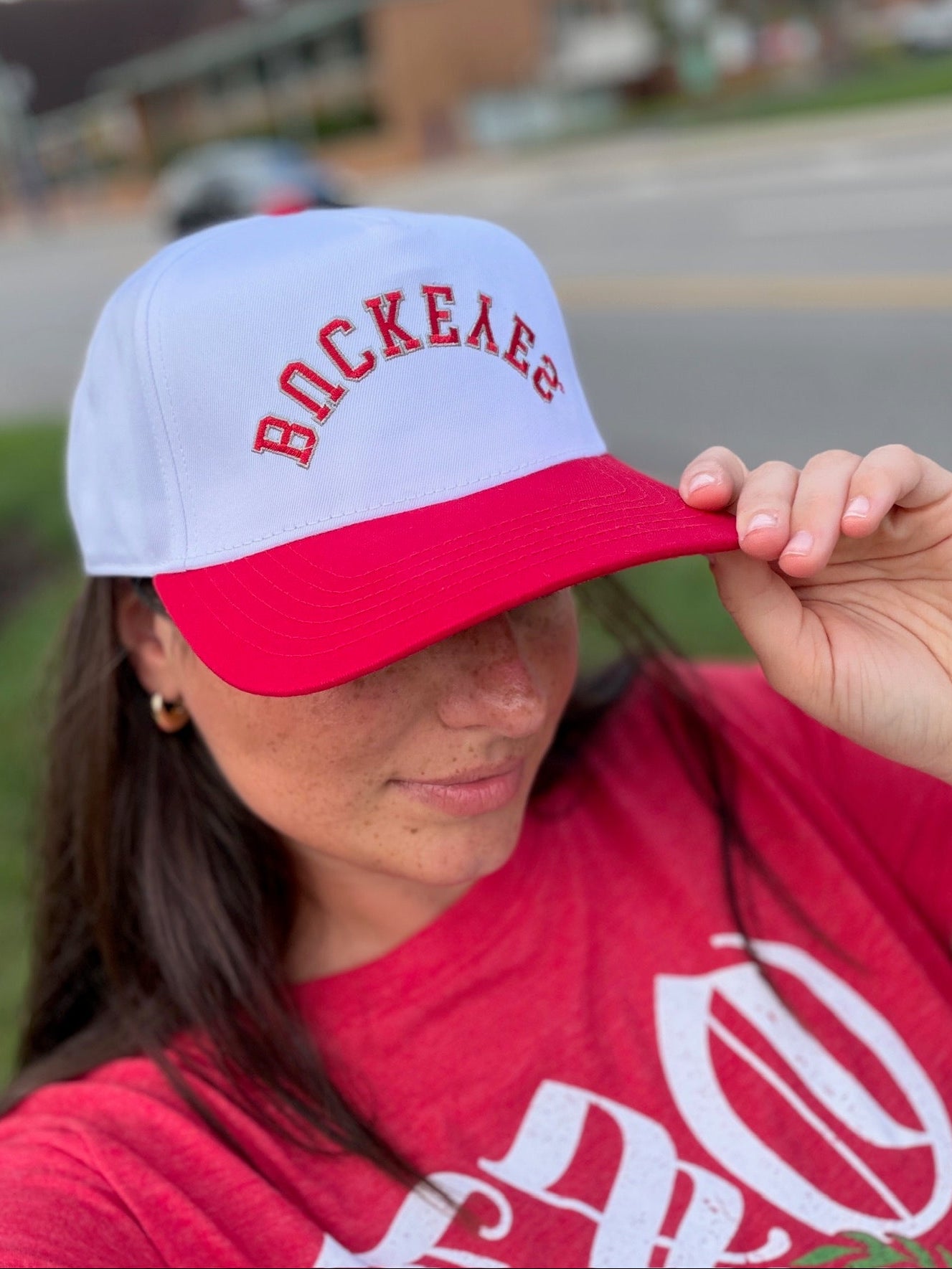 A woman wearing a white and red trucker hat with 'Buckeyes' embroidered red arched text, lifestyle